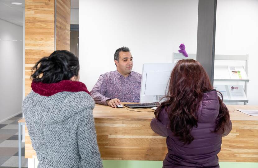 Twee mensen staan aan balie, baliemedewerker staat achter een computer.