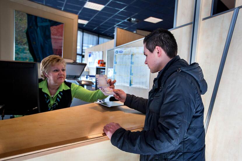 Een jongen aan de balie laat paspoort zien aan vrouwelijke baliemedewerker.